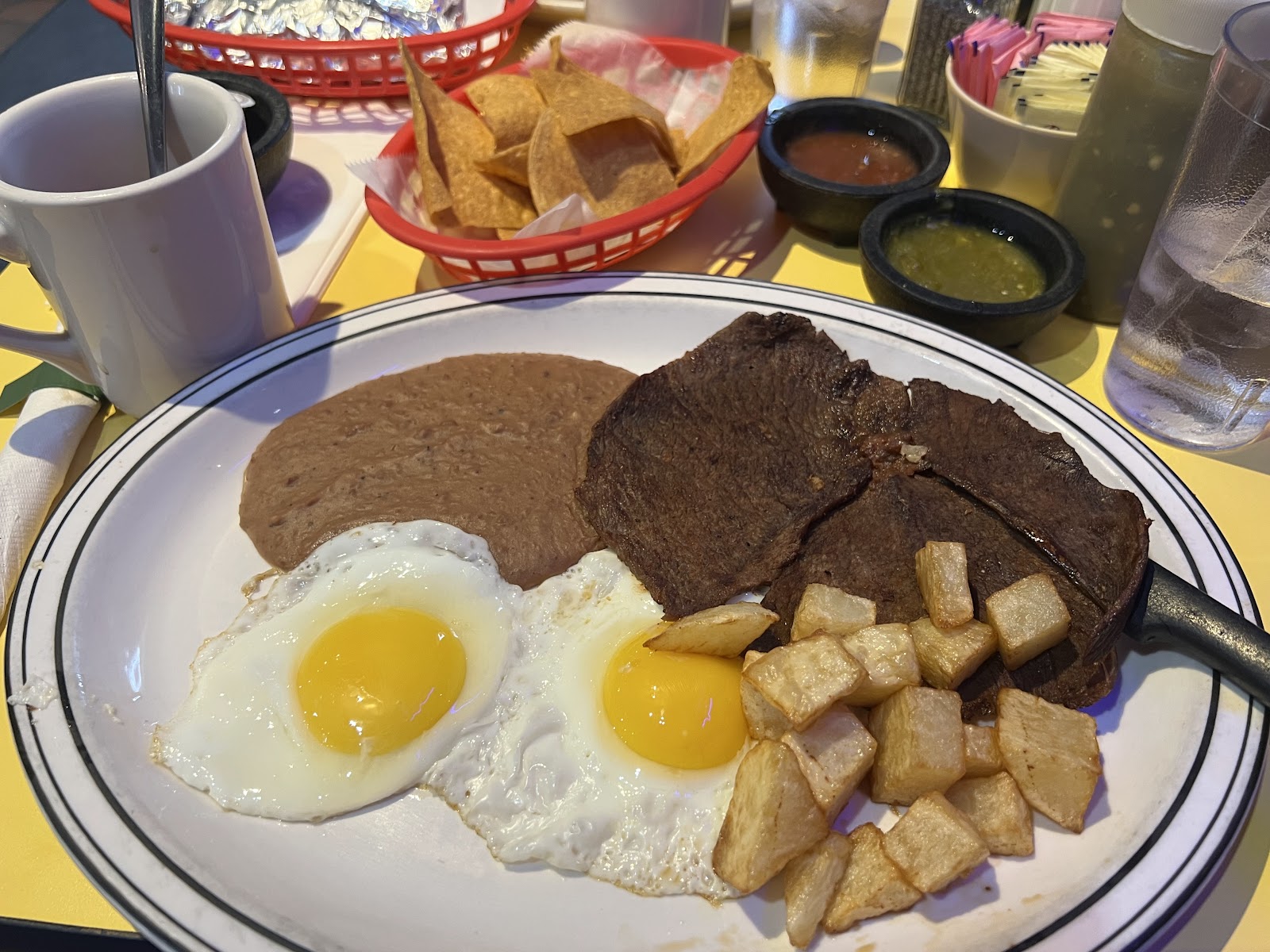 Carne asada breakfast plate with fried eggs, refried beans, and papas