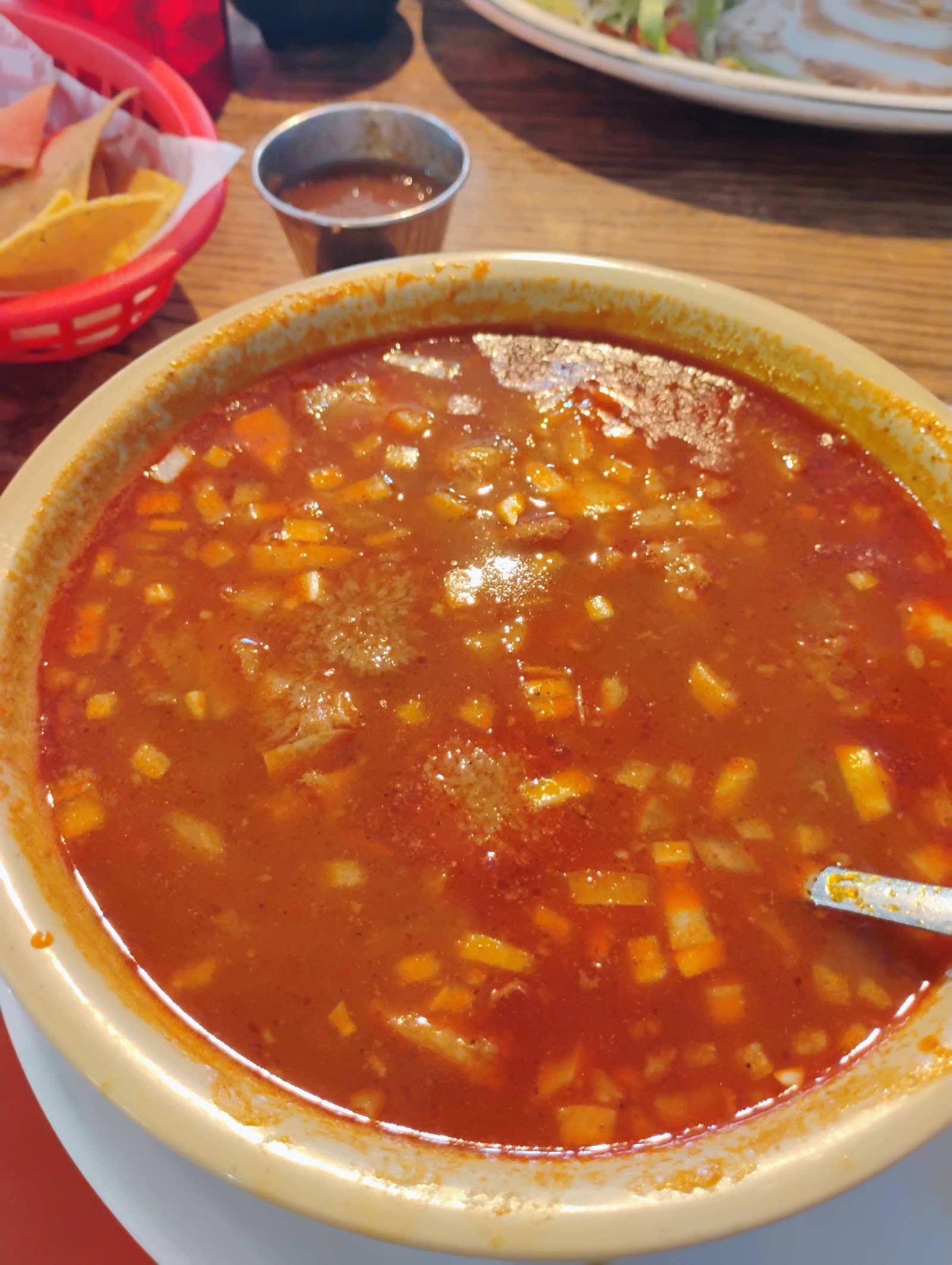 Bowl of red caldo soup served with tortilla chips and salsa